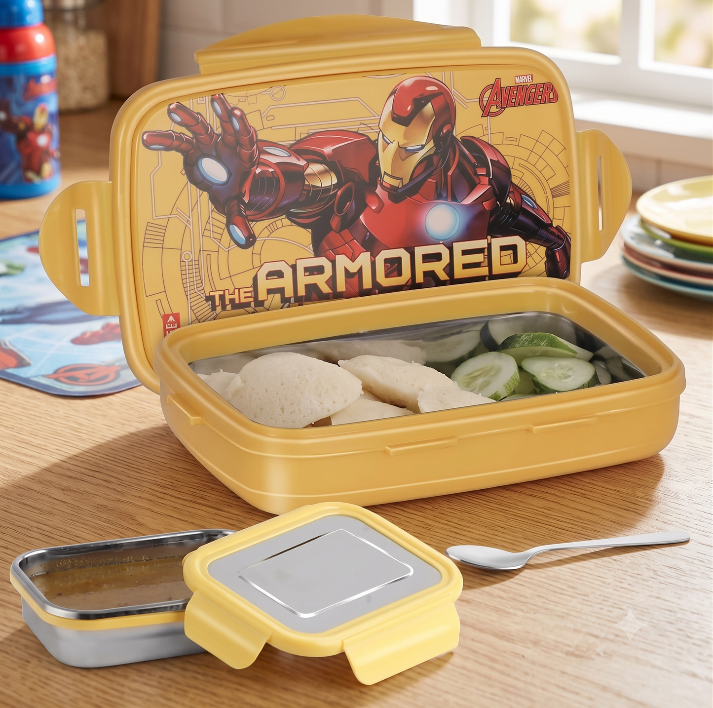 A yellow Marvel-themed lunch box set on a wooden table, shown open with food inside and the lid featuring Iron Man artwork. A separate lid and spoon are placed in front.
